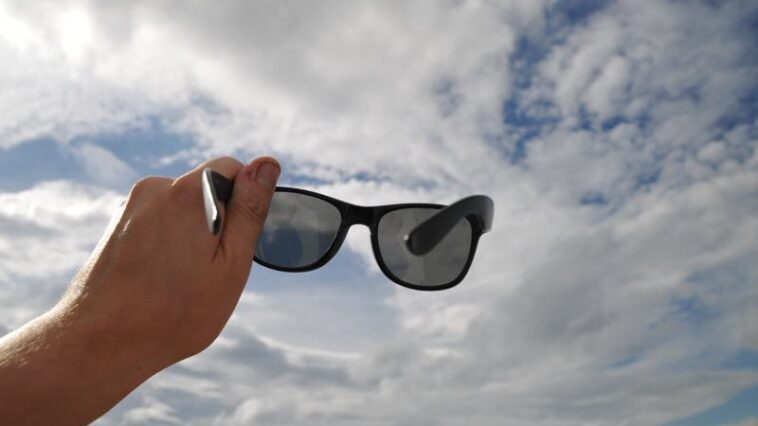 Sonnenbrille wird in Richtung Wolken gehalten