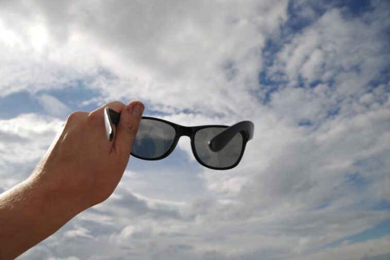Sonnenbrille wird in Richtung Wolken gehalten